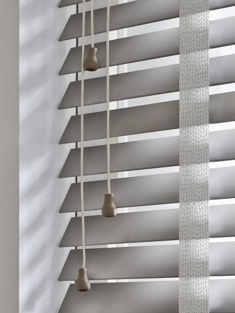 Close-up of angled grey blind slats with hanging pull cords